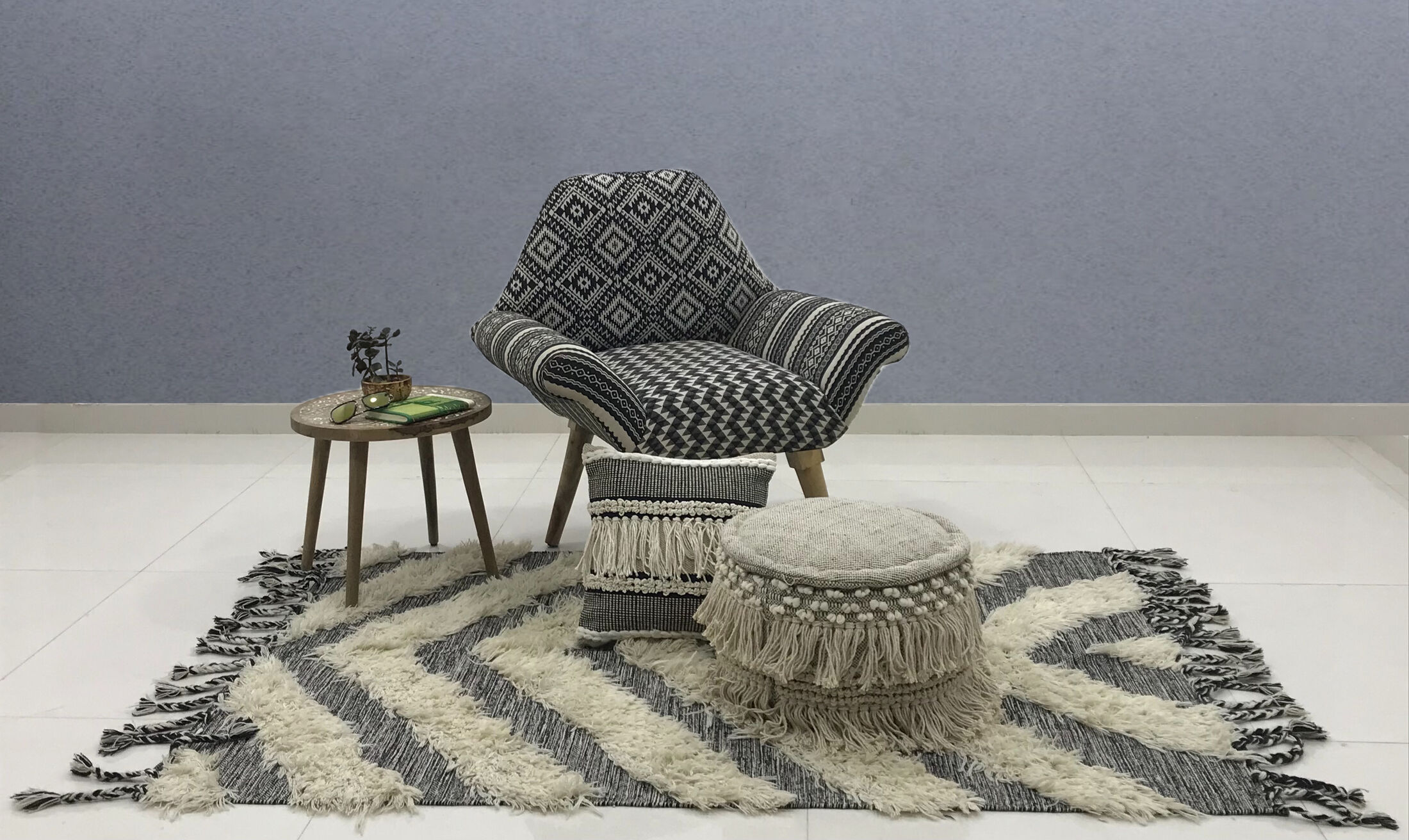 Armchair upholstered in black and white kilim fabric, styled with a handwoven rug, cushion and pouf